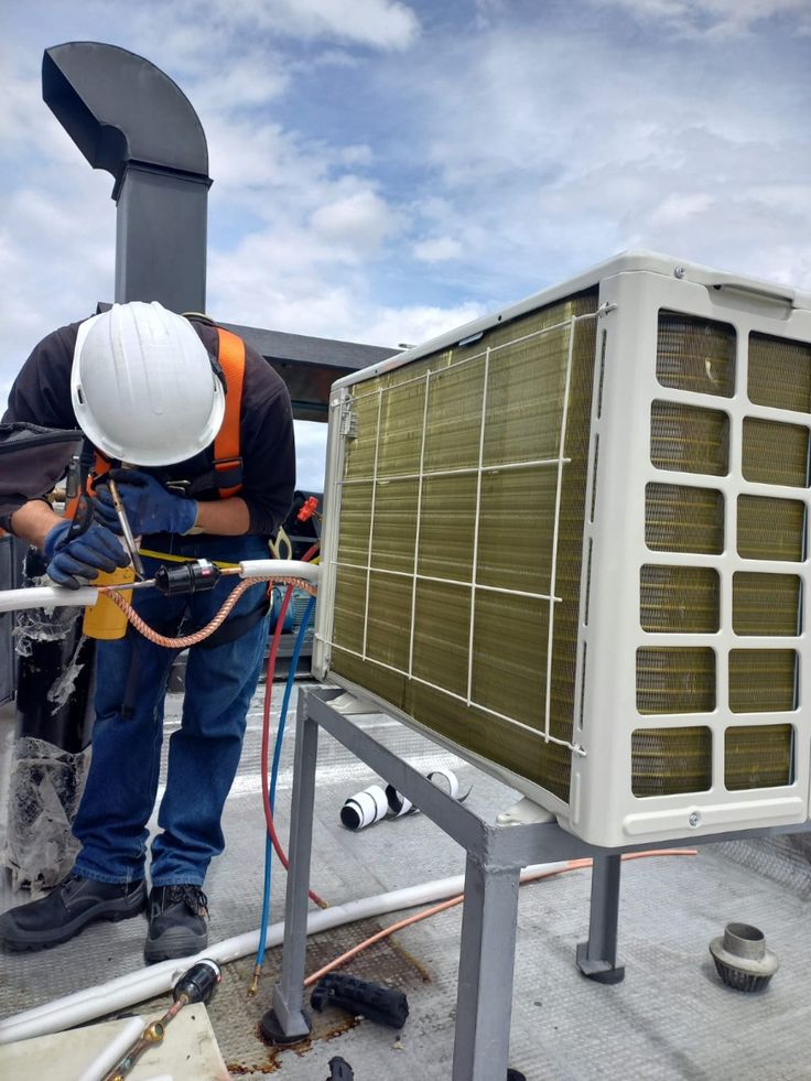 Technician in safety harness brazing refrigerant lines on an outdoor condensing unit