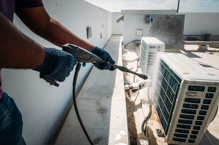 Technician pressure-washing outdoor condensing unit coils during a maintenance visit